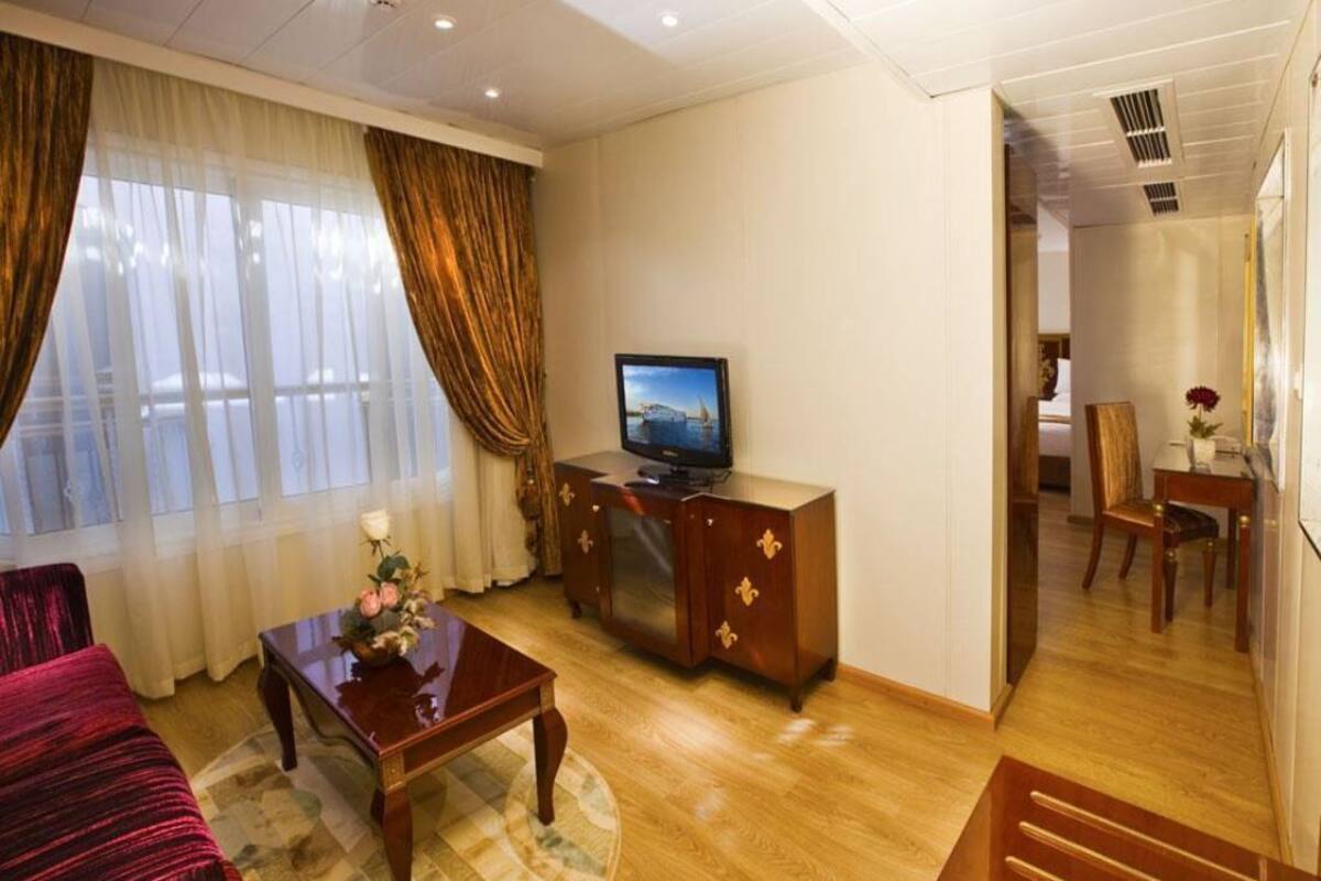 Habitación de hotel con piso de madera, sofá, mesa de centro, televisor y zona de comedor con una silla y una mesa.