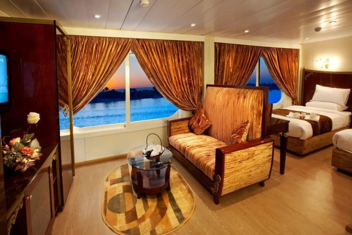 Una habitación de hotel con un ventanal grande, un sofá, una cama, una mesita y un televisor.