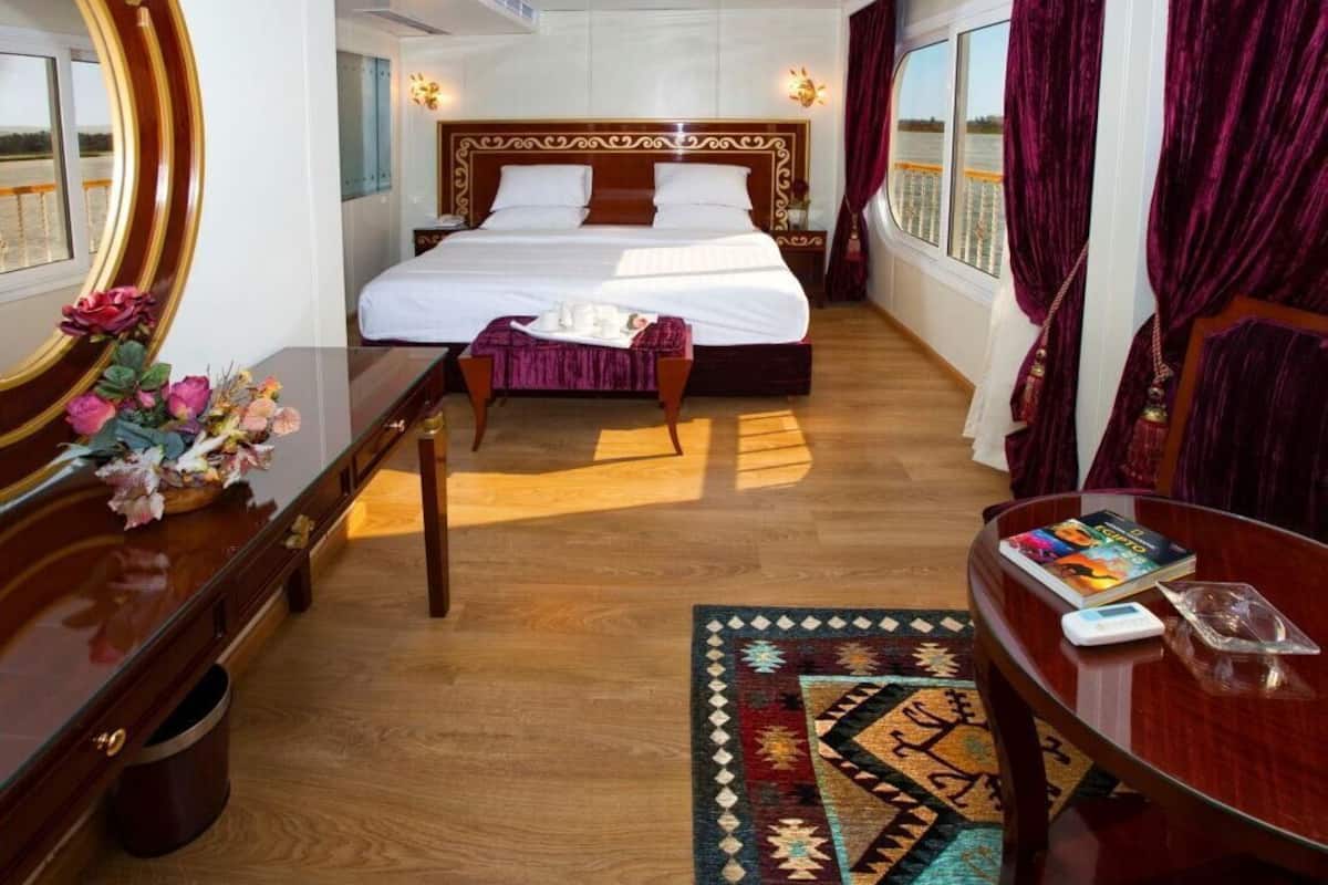 Habitación de hotel con una cama grande, un escritorio de madera, una mesita de noche con un florero y vistas al agua.
