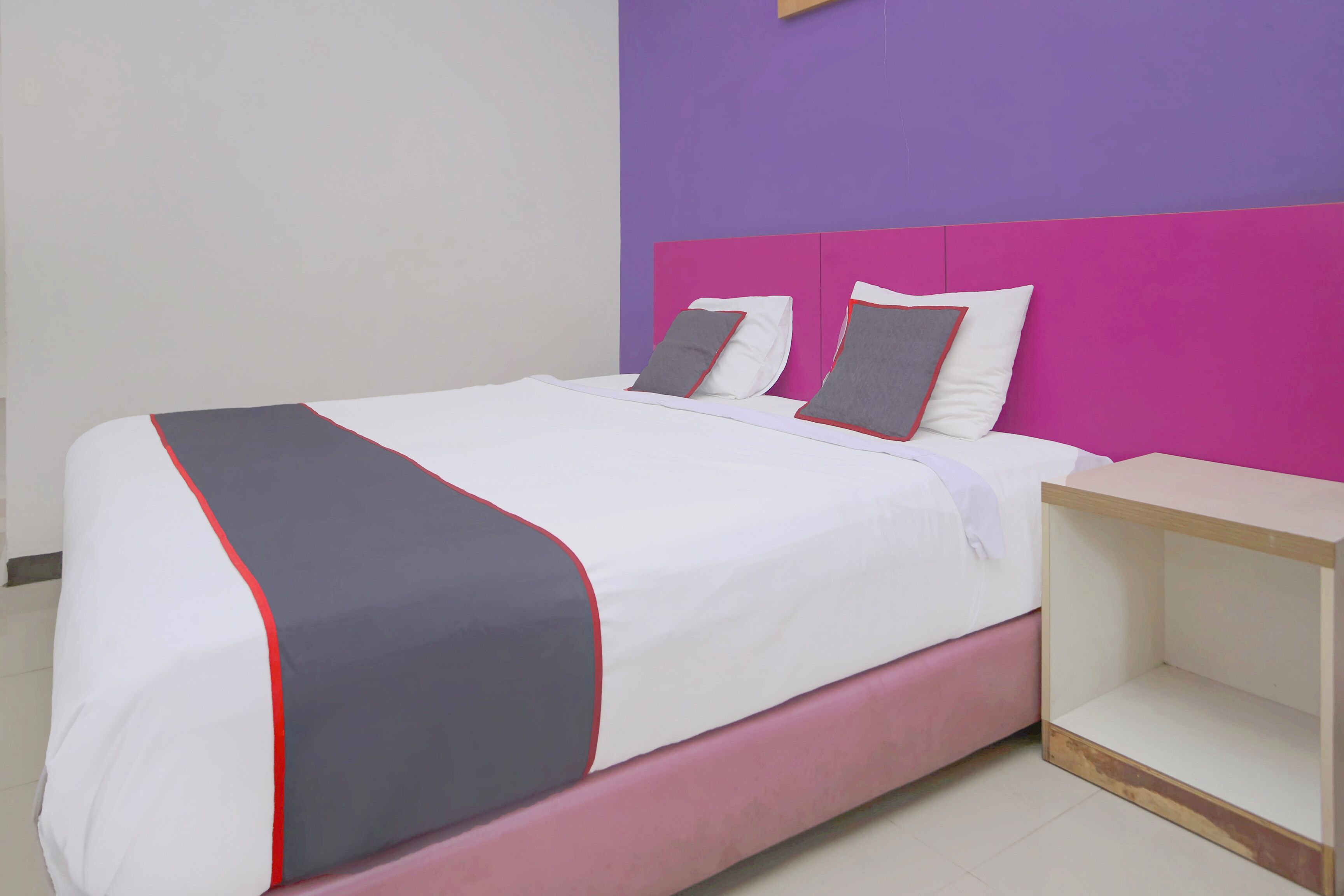 A bed with a white and grey bedspread, two pillows, and a wooden nightstand.