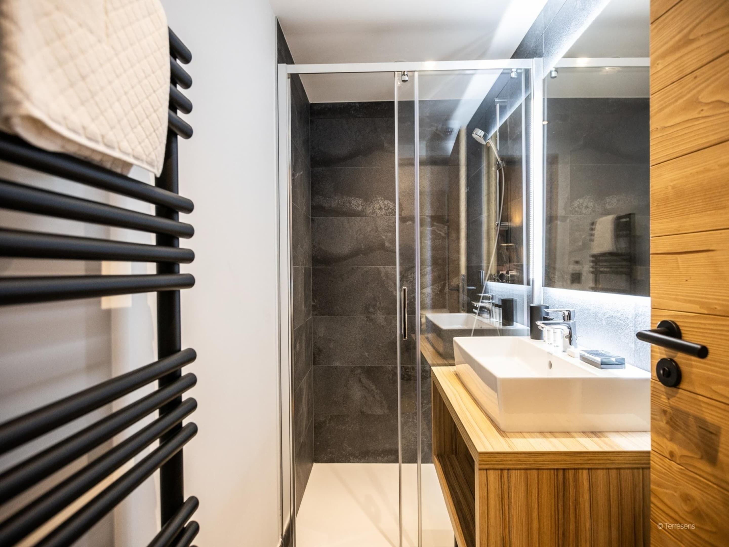 A modern bathroom with a glass shower enclosure, a wooden vanity, and a towel rack.