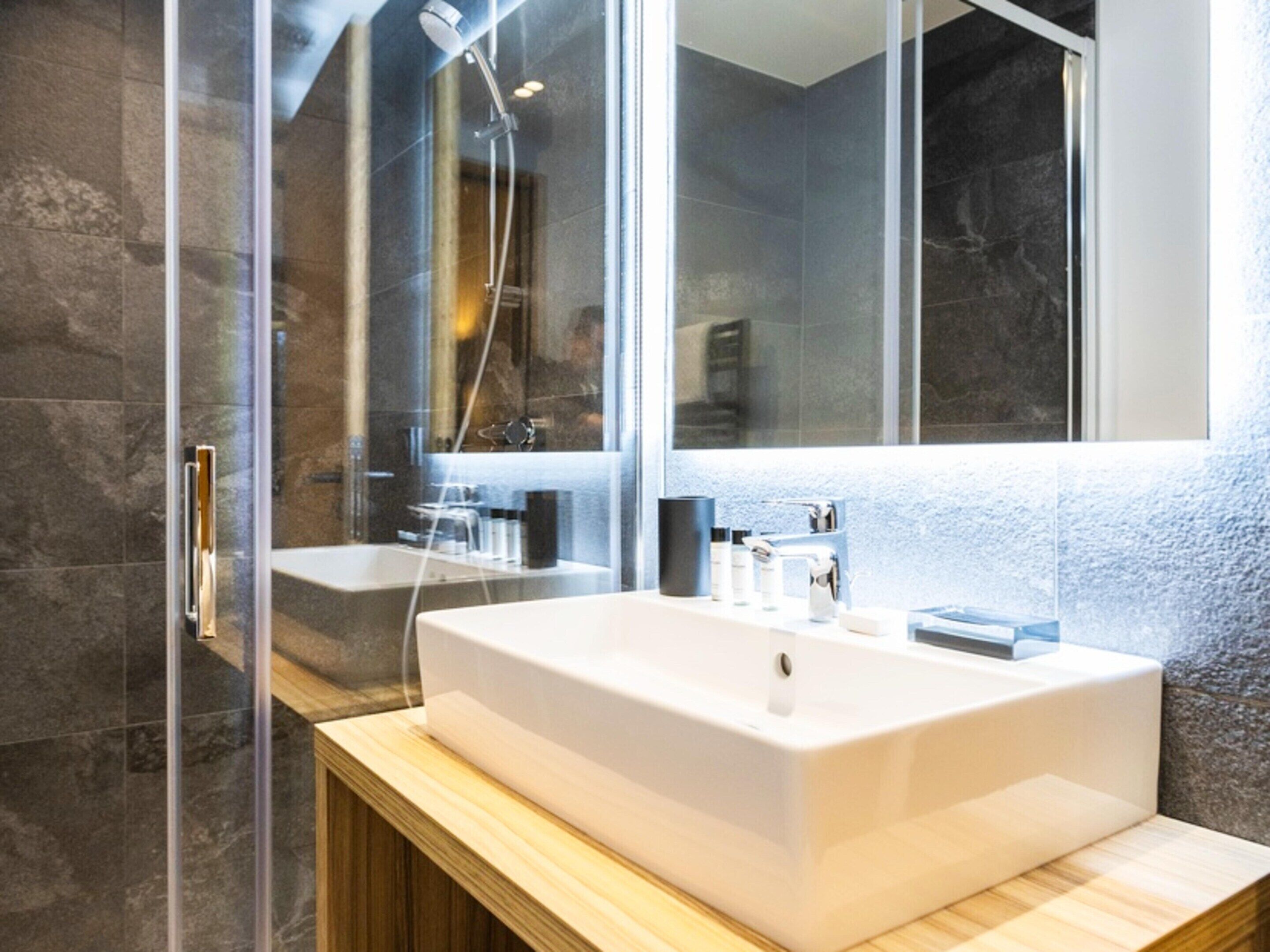 A modern bathroom with a large white sink, a glass shower enclosure, and a large mirror.