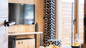 A modern room with a wooden interior, a flat-screen TV mounted on the wall, a dining table with a tray of breakfast items, and a window with blinds. - Apartment in La Chapelle Near Cret-beni Lift (La Chapelle-d'Abondance)