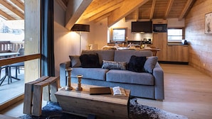 A cozy cabin interior with a wooden ceiling, a sofa, a coffee table, and a kitchen area.