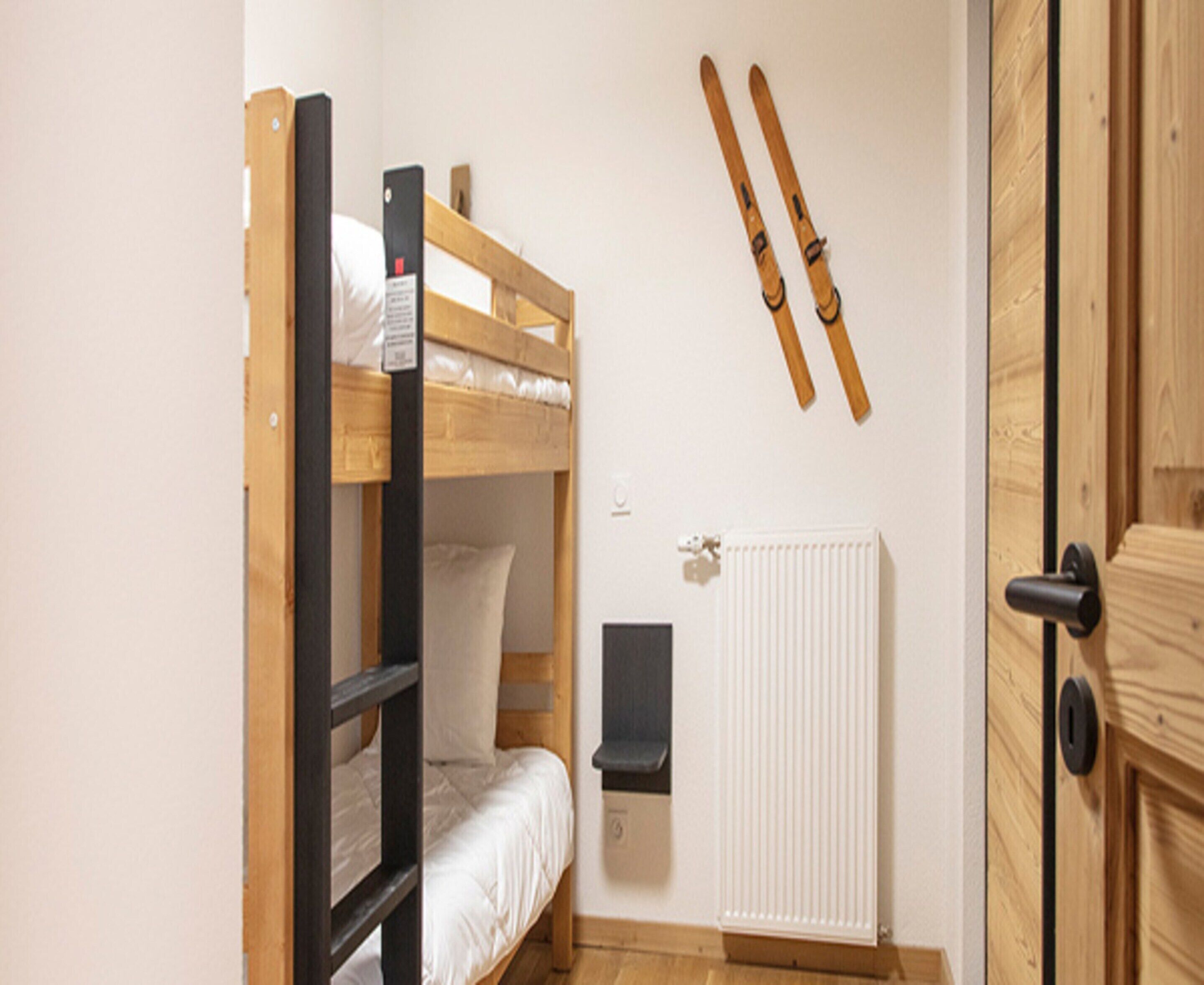 Ein Schlafraum mit Etagenbetten, einem Heizkörper, einer Tür und Skiern, die an der Wand hängen.