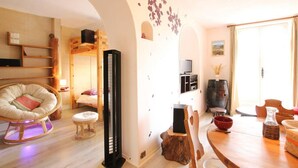 A cozy living room with a wooden floor, a round dining table, a comfortable chair, a black standing heater, a television, and a wooden cabinet. - 1st floor, balcony, tv, 40m², Serre Chevalier (Briançon)