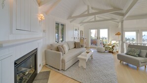 A spacious living room with a fireplace, a large sofa, a coffee table, and a view of the city through large windows.