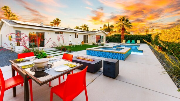 A modern outdoor patio with a dining table, red chairs, a fire pit, and a pool area. - 25% Off 30+ Stay! Prime Location Private Pool, Spa (Palm Springs)