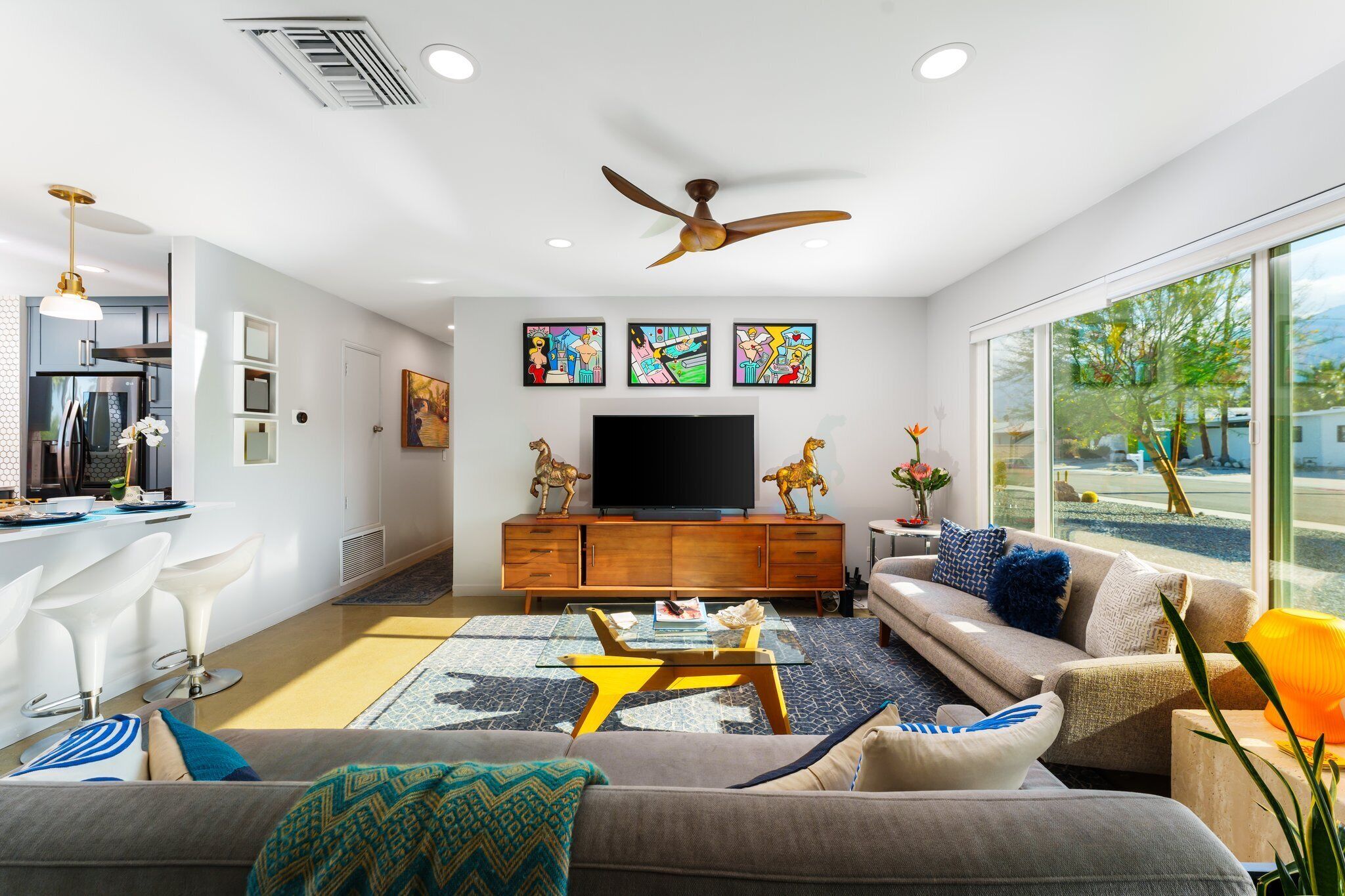 A modern living room with a sofa, coffee table, and TV. There is a dining area with a kitchen in the background.