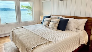 Ein Schlafzimmer mit einem großen Bett, Blick auf das Wasser und einer Deckenleuchte.