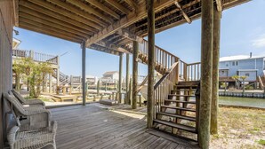 A wooden deck with a wicker chair, a staircase, and a view of houses and water. - Canal-front, Boat Dock, Sleeps 9 - Anchor Eways (Dauphin Island)