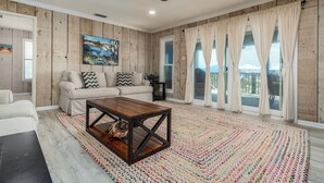 A spacious living room with a wooden ceiling fan, a beige sofa with patterned cushions, a wooden coffee table, and a colorful rug. - Canal-front, Boat Dock, Sleeps 9 - Anchor Eways (Dauphin Island)