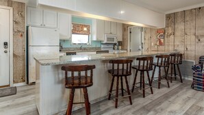 A kitchen with white cabinets, a central island with bar stools, a microwave, and a refrigerator. - Canal-front, Boat Dock, Sleeps 9 - Anchor Eways (Dauphin Island)