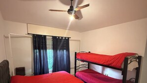 Quarto com beliches, ventoinha no teto, janela com cortinas e porta.
