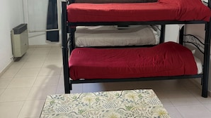 Quarto estilo dormitório com beliches, ventilador de teto, radiador e tapete estampado.