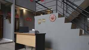A reception desk with a computer, a clock, and a staircase. - Hotel O Palembang Near Bumi Sriwijaya Stadium Formerly HPA Homestay (Palembang)