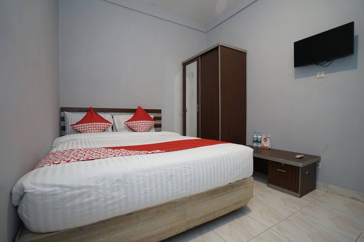 A bedroom with a bed, a wardrobe, a desk, and a television mounted on the wall.