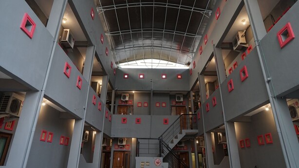 A multi-level interior with a central staircase, red square frames on walls, and a grid-like ceiling structure. - Hotel O Palembang Near Bumi Sriwijaya Stadium Formerly HPA Homestay (Palembang)