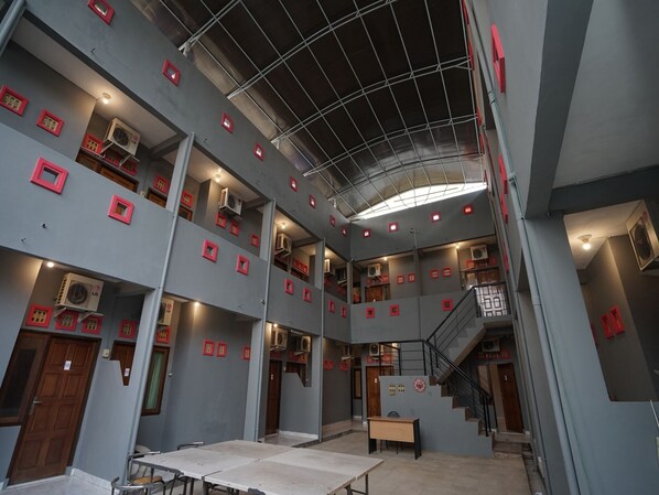 Ein mehrgeschossiges Interieur mit einer zentralen Treppe, mehreren Klimaanlagen und einer Reihe kleiner Fenster mit roten Rahmen.