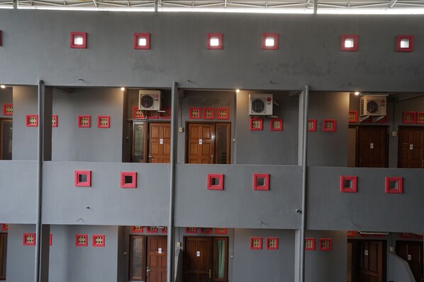 Un edificio de varios pisos con balcones, unidades de aire acondicionado y ventanas con marcos rojos.