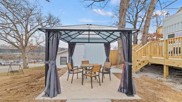 A covered patio area with a table and chairs, surrounded by trees and a wooden deck. - UNIQUE COUPLES GETAWAY: Rooftop Deck, Branson Landing, Trolley Stop (Branson)
