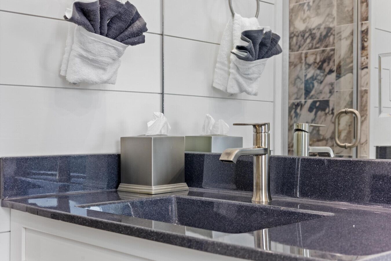 Une salle de bain moderne avec un comptoir en granit, un robinet argenté et deux distributeurs de serviettes.