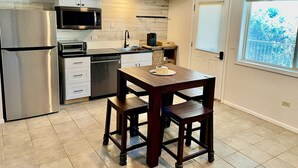 A compact kitchen with a stainless steel refrigerator, a microwave, and a sink. There is a wooden table with two chairs. - Spa Studio Retreat w/ Lake Access + Sauna & Jacuzzi (Kimberling City)