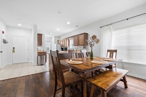 A modern kitchen with wooden cabinets, a dining area with a large wooden table and chairs, and a view of the living room.