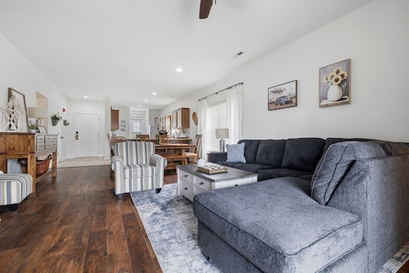 A spacious living room with a grey sectional sofa, a striped armchair, and a dining area with wooden furniture.