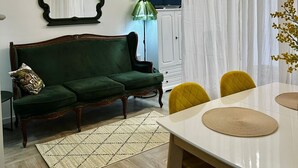 A living room with a green sofa, a dining table with yellow chairs, a TV, and a large mirror on the wall. - Charming apartment with WiFi, AC in fabulous Bar (Bar)