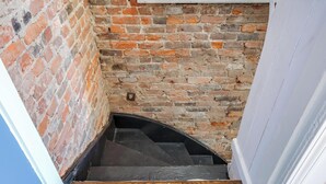 Un escalier étroit, avec un mur de briques d’un côté et une porte blanche de l’autre.