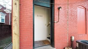 Un bâtiment en briques rouges, doté d’une porte en bois portant le numéro « 2 » et d’un petit seuil menant à un intérieur blanc.