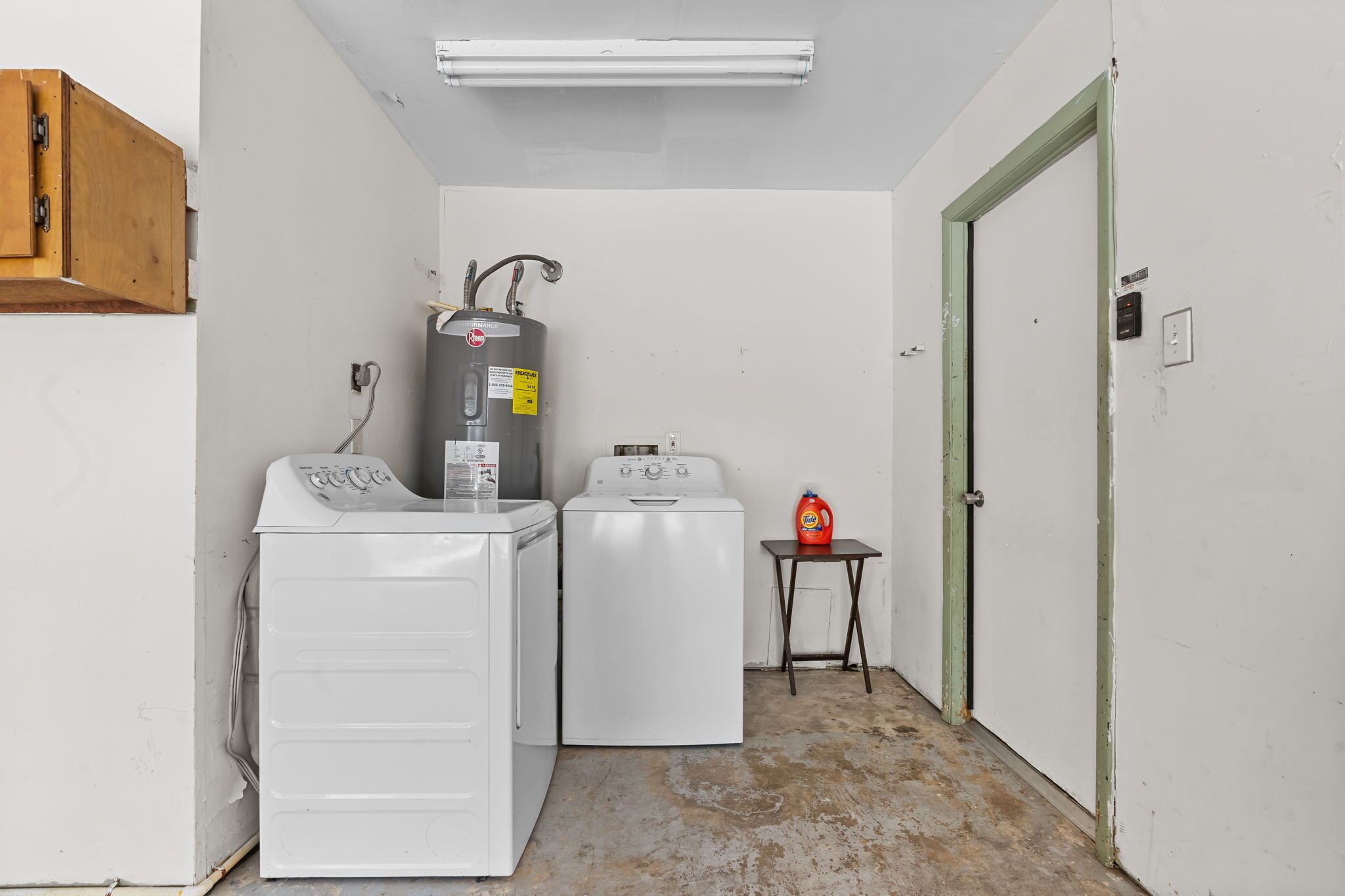 A laundry room with two white washers and a dryer, a water heater, and a small table with a detergent bottle.