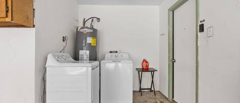 A laundry room with two white washers and a dryer, a water heater, and a small table with a detergent bottle.