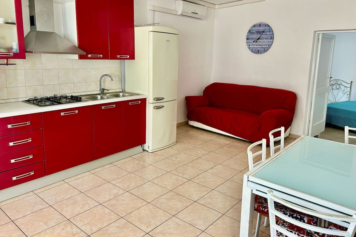 A compact kitchen with red cabinets, a white refrigerator, and a dining area with a table and chairs.