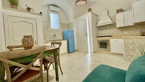 A compact kitchen with white cabinets, a blue refrigerator, and a dining area with a wooden table and chairs. - Corte Regi Appartment (Gallipoli)