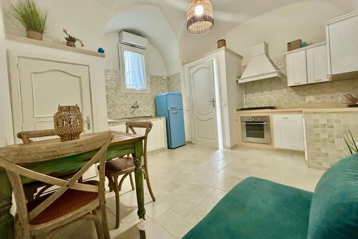 A compact kitchen with white cabinets, a blue refrigerator, and a dining area with a wooden table and chairs.