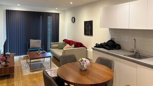 Uma sala de estar moderna com sofá, mesa de centro e mesa de jantar. Há uma área de cozinha com pia e armários.