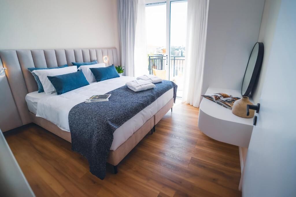 A modern bedroom with a large bed, a bedside table, a mirror, and a view of the outdoors.