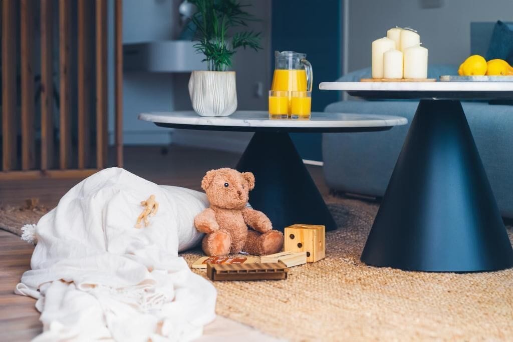 Una habitación acogedora con una cama, un osito de peluche, una mesita con velas y limones, y una planta en maceta.