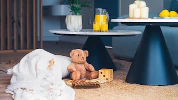 Ein gemütliches Zimmer mit einem Bett, einem Teddybären, einem kleinen Tisch mit Kerzen und Zitronen sowie einer Topfpflanze.