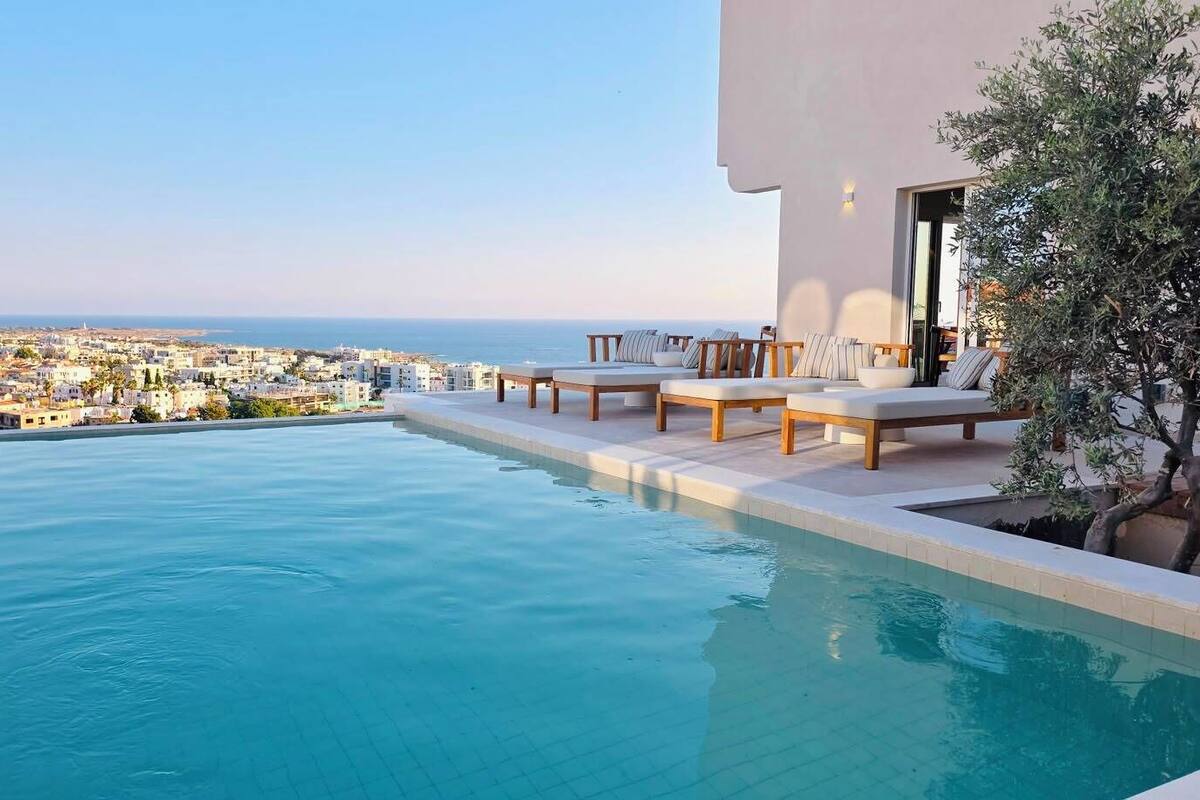 Uma piscina infinita no terraço com espreguiçadeiras e vista para a cidade.