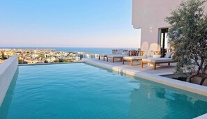 A rooftop infinity pool with lounge chairs and a view of the cityscape.