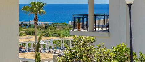 A resort with a view of the ocean, featuring a pool area, palm trees, and a tiled roof.