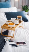 A neatly made bed with white bedding and blue pillows, a tray with breakfast items, and an open magazine on the bed.