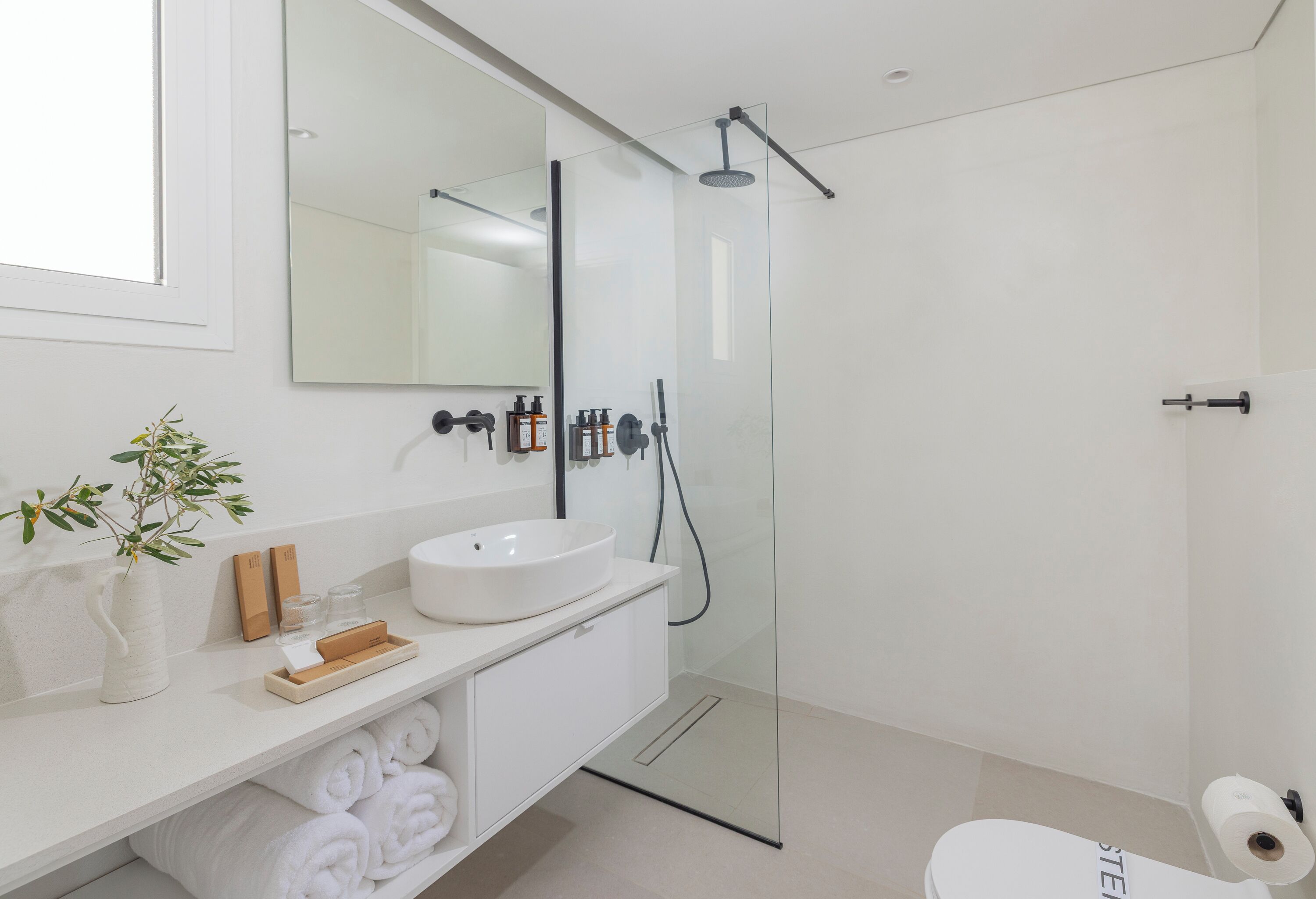 Un baño moderno con lavamanos blanco, espejo y cabina de ducha con mampara de vidrio.