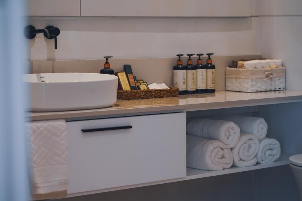 A bathroom with a white sink, toiletries, towels, and a basket.
