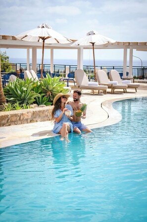 A couple sitting by a pool with umbrellas and lounge chairs in the background. - WellClub Resort - Suites & Wellness (Chlorakas)