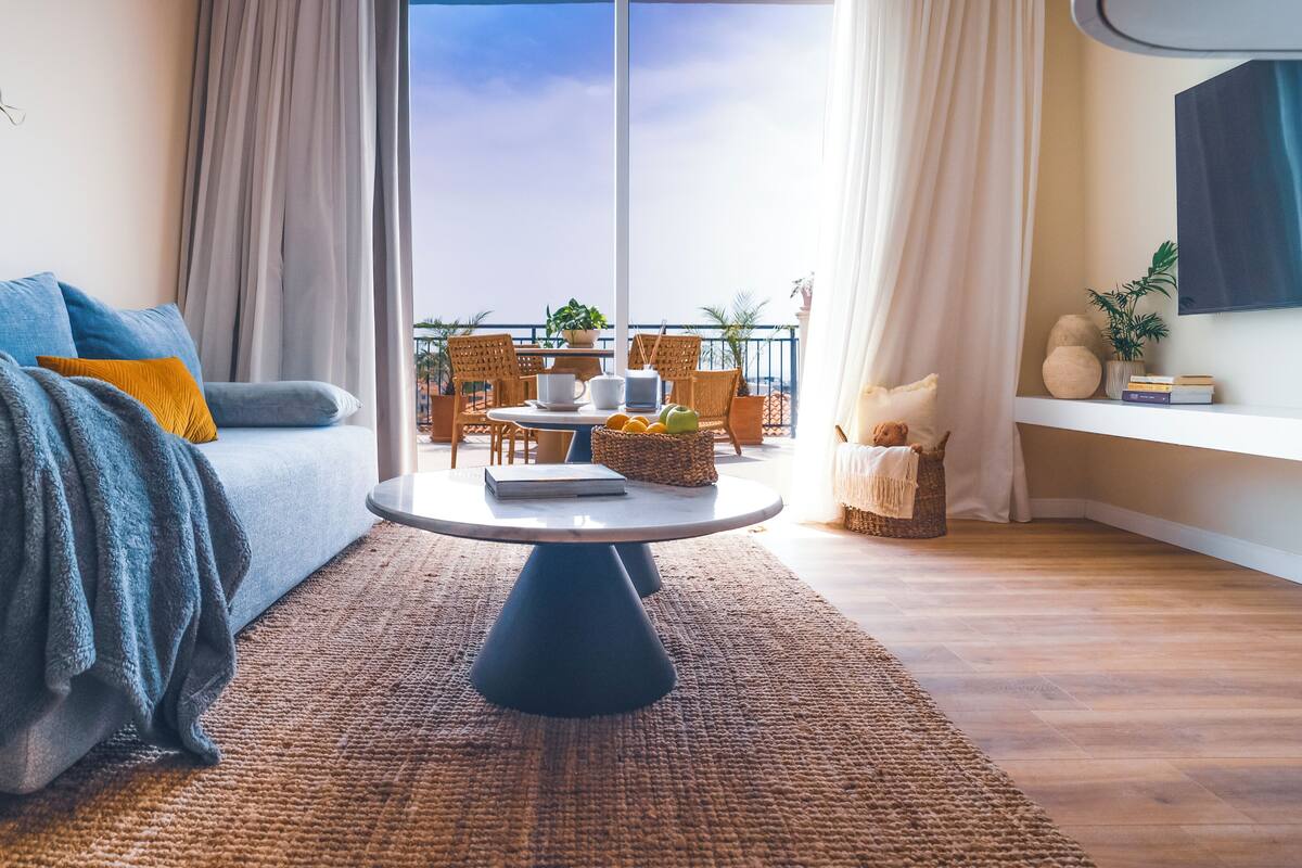 Uma sala de estar moderna com um sofá, uma mesa de centro e vista para uma varanda com mobiliário externo.