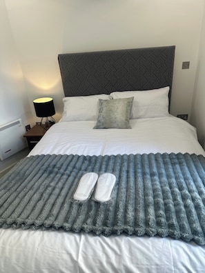 A neatly made bed with white linens, a grey headboard, and a grey throw blanket with slippers on it. - Riverview - Balcony - 4 Guests - Near Old Trafford (Salford)